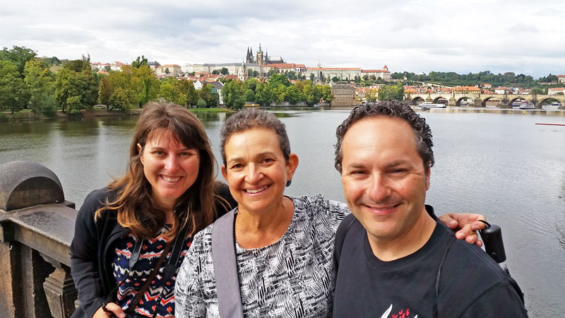 3 people standing on a bridge with prague castle and river in background